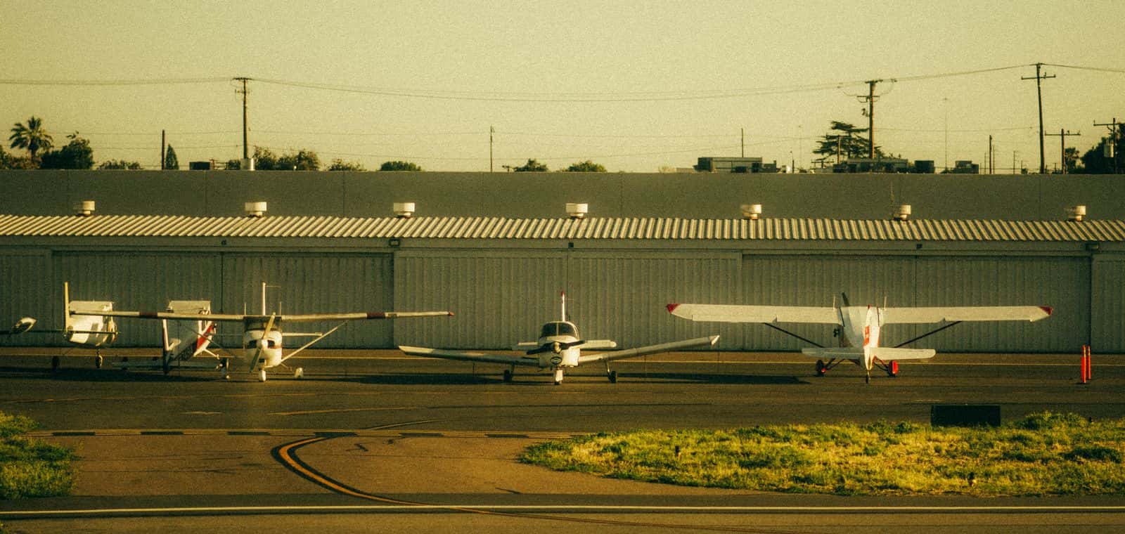 A row of light training aircraft parked in front of the hangars at golden hour